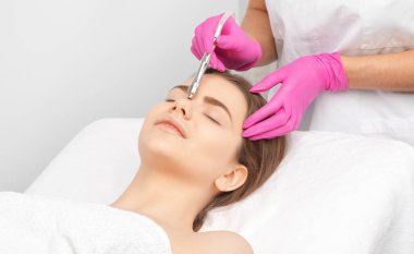 Kozmetik uzmanı, güzellik salonundaki güzel bir kızın yüzünün mikro cilt bakımını yapıyor. Kozmetoloji ve profesyonel cilt bakımı..