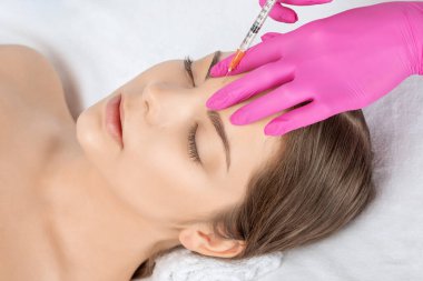 Kozmetik uzmanı güzel bir kadının yüzüne kırışıklık önleyici iğneler yapıyor. Güzellik salonunda kadın estetiği..