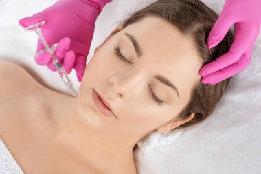 Kozmetik uzmanı güzel bir kadının yüzüne kırışıklık önleyici iğneler yapıyor. Güzellik salonunda kadın estetiği..