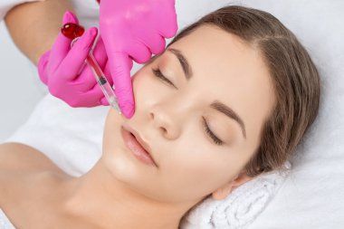 Kozmetik uzmanı, güzel bir kadının burun kıvrımlarında dudak büyütme ve kırışıklık önleyici iğneler yapar. Güzellik salonunda kadın kozmetolojisi.