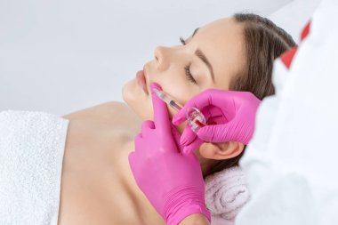 Kozmetik uzmanı, güzel bir kadının burun kıvrımlarında dudak büyütme ve kırışıklık önleyici iğneler yapar. Güzellik salonunda kadın kozmetolojisi.