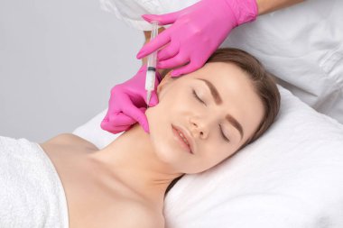 Kozmetik uzmanı, bir kadının çenesinde, yanaklarında ve boynunda çift çeneye karşı yağ yakmak için lipolitik enjeksiyon yapar. Güzellik salonunda kadın estetiği. Kozmetoloji konsepti..