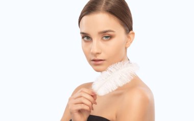 Güzel esmer bir kızın portresi. Elinde beyaz bir tüy, sağlıklı ve temiz bir cildi ve taze bir makyajı var. Estetik kozmetoloji ve makyaj konsepti.