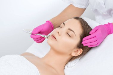 Kozmetik uzmanı yüzünde sivilce ve göz kenarındaki siyah noktalara karşı mikro dermabrüksiyon uygular. Güzellik salonunda kadın kozmetolojisi.