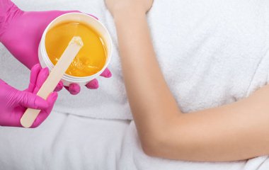 Güzellik uzmanı bir güzellik salonunda bir kadının kollarının şeker macununu tükürür..