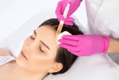 Kozmetik uzmanı güzellik salonunda güzel bir kadının yüzü üzerinde terapi uygular. Kozmetoloji kavramı.