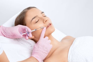 Kozmetik uzmanı, güzel bir kadının burun kıvrımlarında dudak büyütme ve kırışıklık önleyici iğneler yapar. Güzellik salonunda kadın kozmetolojisi.