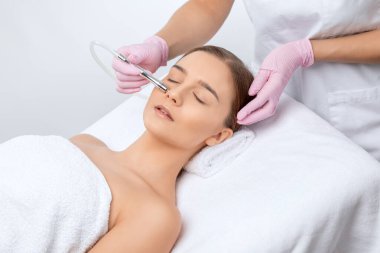 Kozmetik uzmanı, güzellik salonundaki güzel bir kızın yüzünün mikro cilt bakımını yapıyor. Kozmetoloji ve profesyonel cilt bakımı..