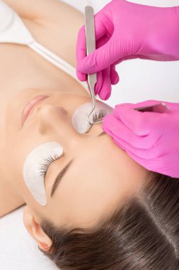 Güzellik salonunda uzun kirpikleri olan güzel bir kadın. Kirpik uzatma prosedürü. Kırbaçlar yakın.