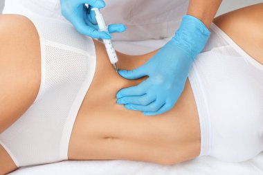 Kozmetik uzmanı bir kadının karnında ve belinde yağ yakmak için lipolitik enjeksiyon yapar. Güzellik salonunda kadın estetiği. Kozmetoloji konsepti..