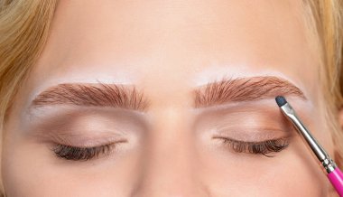 Makyaj sanatçısı kaşlar için beyaz kalemle işaretler yapar ve kaşları boyar. Profesyonel makyaj ve yüz bakımı.