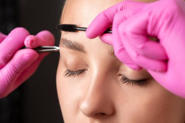 Makyöz, güzellik salonunu boyadıktan sonra kaşlarını tarar ve koparır. Profesyonel makyaj ve kozmetoloji cilt bakımı..