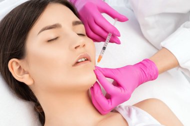 Kozmetik uzmanı, güzel bir kadının burun kıvrımlarında dudak büyütme ve kırışıklık önleyici iğneler yapar. Güzellik salonunda kadın kozmetolojisi.