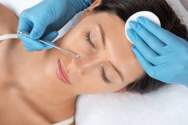 Yüzün siyah noktalarından ve sivilcelerden temizlenmesi için bir prosedür. Kozmetik uzmanı güzellik salonunda genç bir kadının sorunlu cildini tedavi ediyor. Estetik kozmetoloji ve makyaj konsepti.