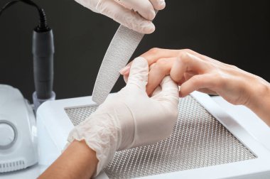 Manikür testeresinin ustası güzellik salonundaki tırnak uzatma işlemi sırasında tırnak şekli takıyor. Eller için profesyonel bakım.