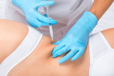 Kozmetik uzmanı bir kadının karnında ve belinde yağ yakmak için lipolitik enjeksiyon yapar. Güzellik salonunda kadın estetiği. Kozmetoloji konsepti..