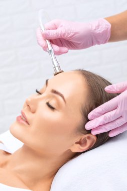 Kozmetik uzmanı, güzellik salonundaki güzel bir kızın yüzünün mikro cilt bakımını yapıyor. Kozmetoloji ve profesyonel cilt bakımı..