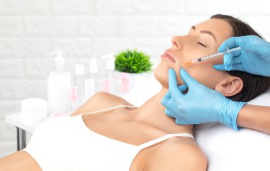 Kozmetik uzmanı güzel bir kadının yüzüne kırışıklık önleyici iğneler yapıyor. Güzellik salonunda kadın estetiği..