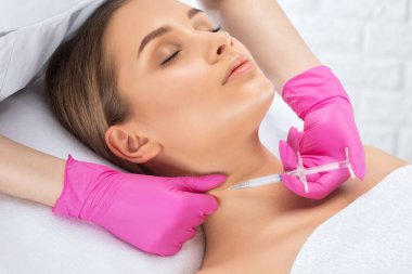 Kozmetik uzmanı, bir kadının çenesinde, yanaklarında ve boynunda çift çeneye karşı yağ yakmak için lipolitik enjeksiyon yapar. Güzellik salonunda kadın estetiği. Kozmetoloji konsepti..