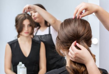 Kuaför, güzellik salonunda siyah bir elbise içinde güzel makyajlı genç ve çekici bir kadına saç stili yapar..
