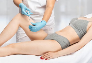 Bir kadının kalçalarında, bacaklarında ve kalçalarında vücut yağlarını yakmak için lipolitik enjeksiyonlar. Güzellik salonunda kadın estetiği..