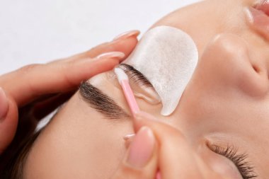 Makyöz, güzellik salonunda güzel bir kadına kirpik boyama ve kaplama prosedürünü uyguluyor. Kirpik uzantıları. Kirpikleri yakın çekim.