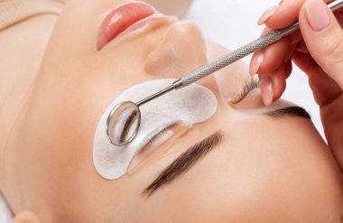 Makyöz, güzellik salonunda güzel bir kadına kirpik boyama ve kaplama prosedürünü uyguluyor. Kirpik uzantıları. Kirpikleri yakın çekim.