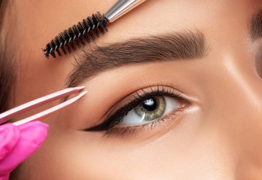Makeup artist plucks eyebrows. Long-lasting styling of the eyebrows and color the eyebrows. Eyebrow lamination. Professional make-up and face care. clipart