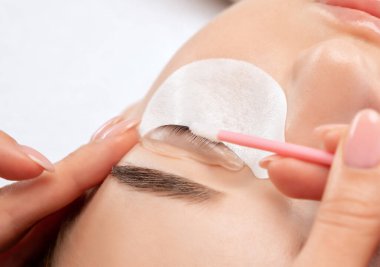 Makyöz, güzellik salonunda güzel bir kadına kirpik boyama ve kaplama prosedürünü uyguluyor. Kirpik uzantıları. Kirpik kaldırılıyor.