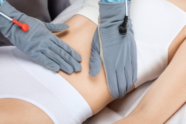 Doktor kozmetik uzmanı güzellik salonundaki güzel bir kızın karnına mikro akım masaj uygular..
