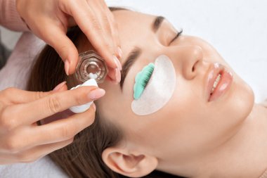 Makyöz, güzellik salonunda güzel bir kadına kirpik boyama ve kaplama prosedürünü uyguluyor. Kirpik uzantıları. Kirpikleri yakın çekim.