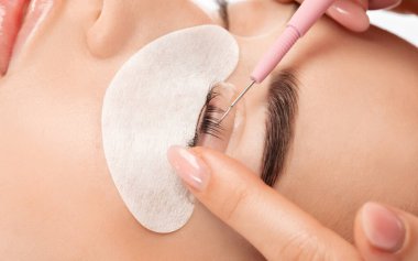 Makyöz, güzellik salonunda güzel bir kadına kirpik boyama ve kaplama prosedürünü uyguluyor. Kirpik uzantıları. Kirpikleri yakın çekim.