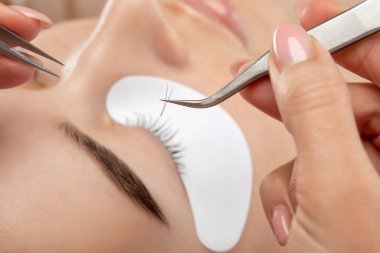 Güzellik salonunda uzun kirpikleri olan güzel bir kadın. Kirpik uzatma prosedürü. Kırbaçlar yakın.