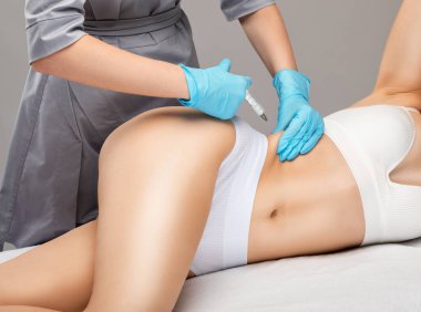 Kozmetik uzmanı bir kadının karnında ve belinde yağ yakmak için lipolitik enjeksiyon yapar. Güzellik salonunda kadın estetiği. Kozmetoloji konsepti..