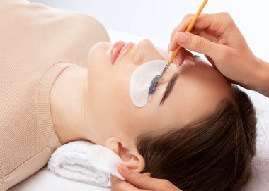 Makyöz, güzellik salonunda güzel bir kadına kirpik boyama ve kaplama prosedürünü uyguluyor. Kirpik uzantıları. Kirpikleri yakın çekim.