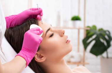 Yüzün siyah noktalarından ve sivilcelerden temizlenmesi için bir prosedür. Kozmetik uzmanı güzellik salonunda genç bir kadının sorunlu cildini tedavi ediyor. Estetik kozmetoloji ve makyaj konsepti.