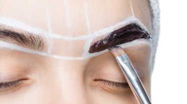 Makyöz, genç bir kızın kınasıyla kaşlarını boyuyor. Güzel kalın kaşlar yakın çekim. Profesyonel makyaj ve kozmetoloji cilt bakımı.