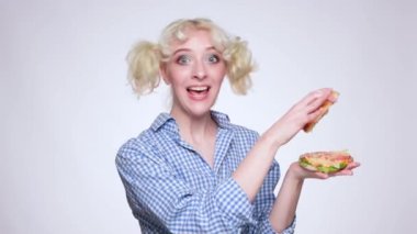 Mavi gömlekli güzel makyajlı genç sarışın bir kız fast food restoranında hamburger yiyor..