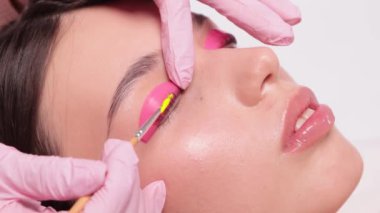 Makyöz, güzellik salonunda güzel bir kadına kirpik boyama ve kaplama prosedürünü uyguluyor. Kirpik uzantıları. Kirpikleri yakın çekim.