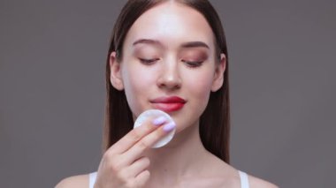 Genç ve güzel bir kız makyajını pamukla temizler ve yüzüne ve gözlerine su döker..