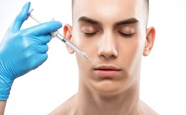 Erkek kozmetolojisi. Güzellik uzmanı genç bir adamın yüzünde gençleştirme enjeksiyon prosedürü uygular..