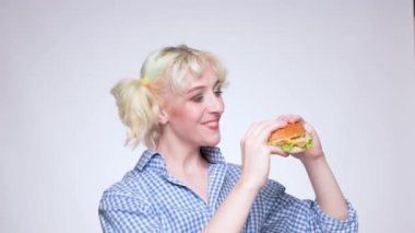 Mavi gömlekli güzel sarışın bir kız elinde pişmiş bir hamburger tutuyor. Fast food.