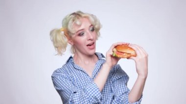 Mavi gömlekli güzel sarışın bir kız elinde pişmiş bir hamburger tutuyor. Fast food.