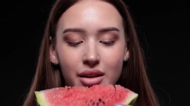 Güzel genç kız olgun sulu bir karpuzu karanlık bir arka planda yer..