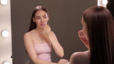 Genç ve güzel bir kız makyajını pamukla temizler ve yüzüne ve gözlerine su döker..