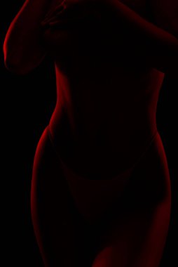 Sıska seksi bir kadın, siyah bir arka planda. Vücudu kırmızı ışıklarla aydınlanıyor..