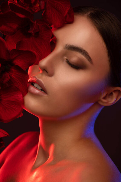 Portrait of attractive girl with healthy clean skin and beautiful make-up. Aesthetic cosmetology and makeup concept.She is holding a red flower in her hands.