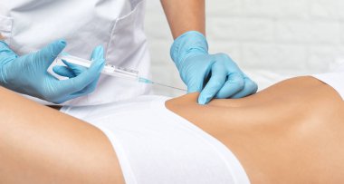 Estetik kozmetik uzmanı bir kadının vücudunda yağ yakmak için lipolitik enjeksiyon yapar. Güzellik salonunda kadın estetiği. Kozmetoloji konsepti..