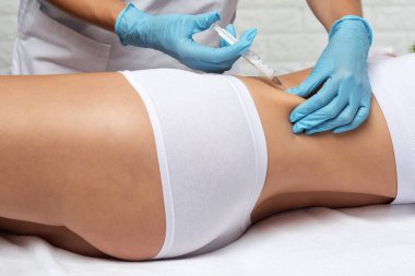 Estetik kozmetik uzmanı bir kadının vücudunda yağ yakmak için lipolitik enjeksiyon yapar. Güzellik salonunda kadın estetiği. Kozmetoloji konsepti..