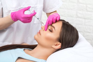 Doktor burundaki tümseği düzeltmek için iğne yapar. Güzellik uzmanı, yüzündeki kırışıklıklara karşı iğne yapar. Güzellik salonunda kadın kozmetolojisi.